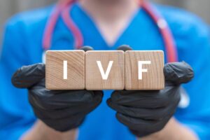 A practitioner in black latex gloves holds up cubes reading “IVF.”