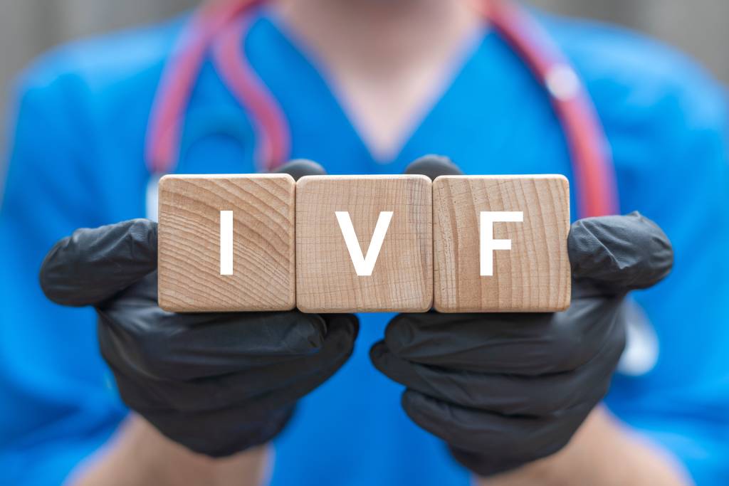 A practitioner in black latex gloves holds up cubes reading “IVF.”
